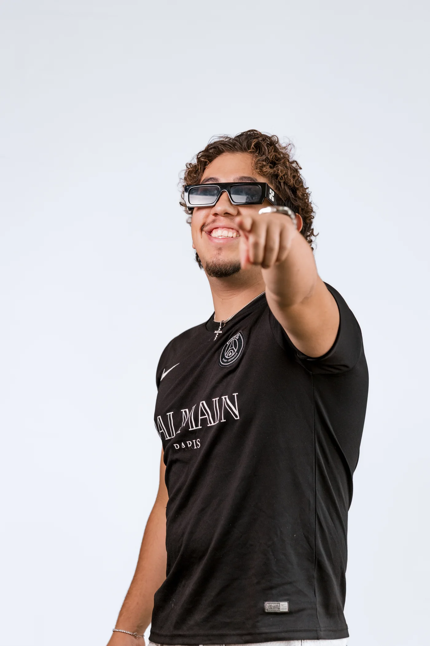 El Panasuyo smiling and pointing at the camera, wearing sunglasses and a black T-shirt